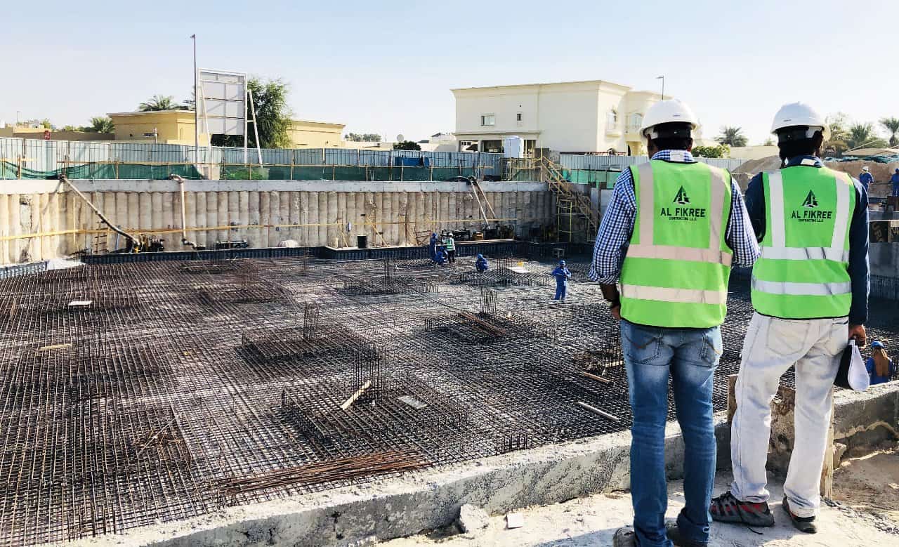 Two men in green vests working on a construction site, focused and determined to complete their tasks.