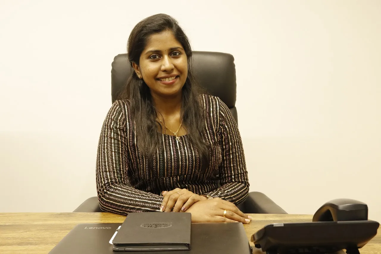 Woman seated at a desk with a laptop and phone, wearing a striped shirt.