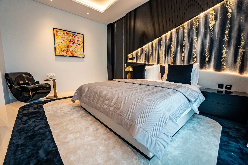 A sleek modern bedroom with a neatly arranged bed, a cozy chair, and artistic wall décor that brings warmth to the room.