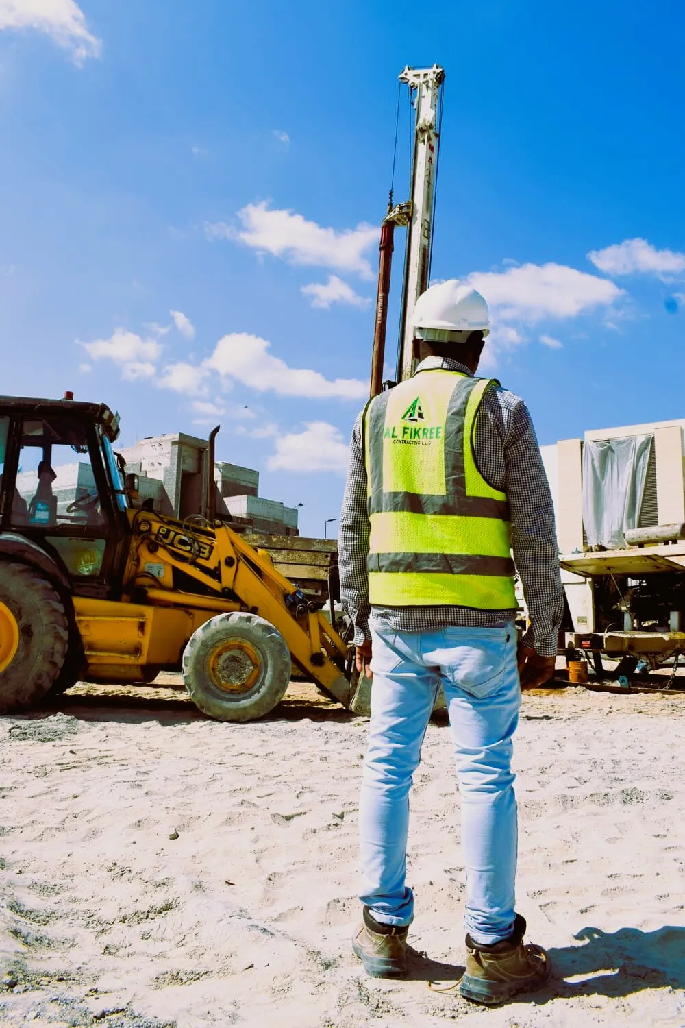 Engineer wearing jacket and safety helmet looking to a constructing building.