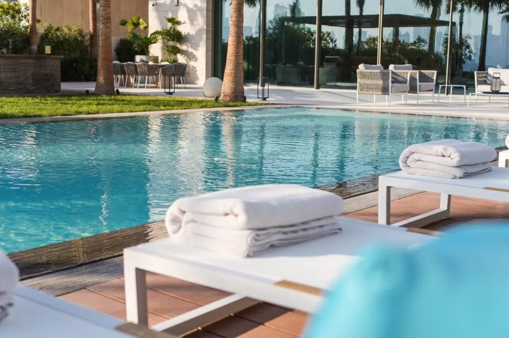 A serene pool scene featuring white lounge chairs and a vibrant blue table, perfect for relaxation and leisure.
