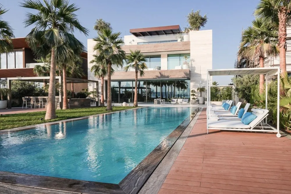 A stylish modern villa with a refreshing pool and swaying palm trees, embodying relaxation and luxury in a tropical setting.