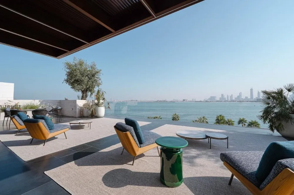 Luxurious outdoor seating area with modern chairs, a green side table, and scenic views of the waterfront and city skyline.