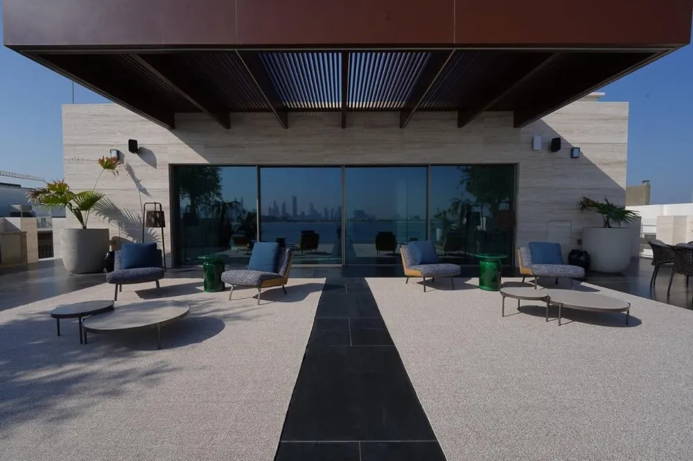 Modern terrace with stylish seating, a green accent table, and expansive glass doors showcasing a city skyline view.