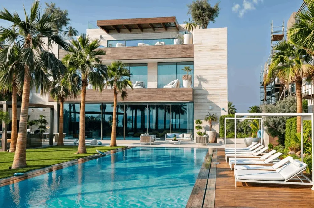 A sleek modern villa featuring a sparkling pool surrounded by lush palm trees, creating a serene tropical oasis.
