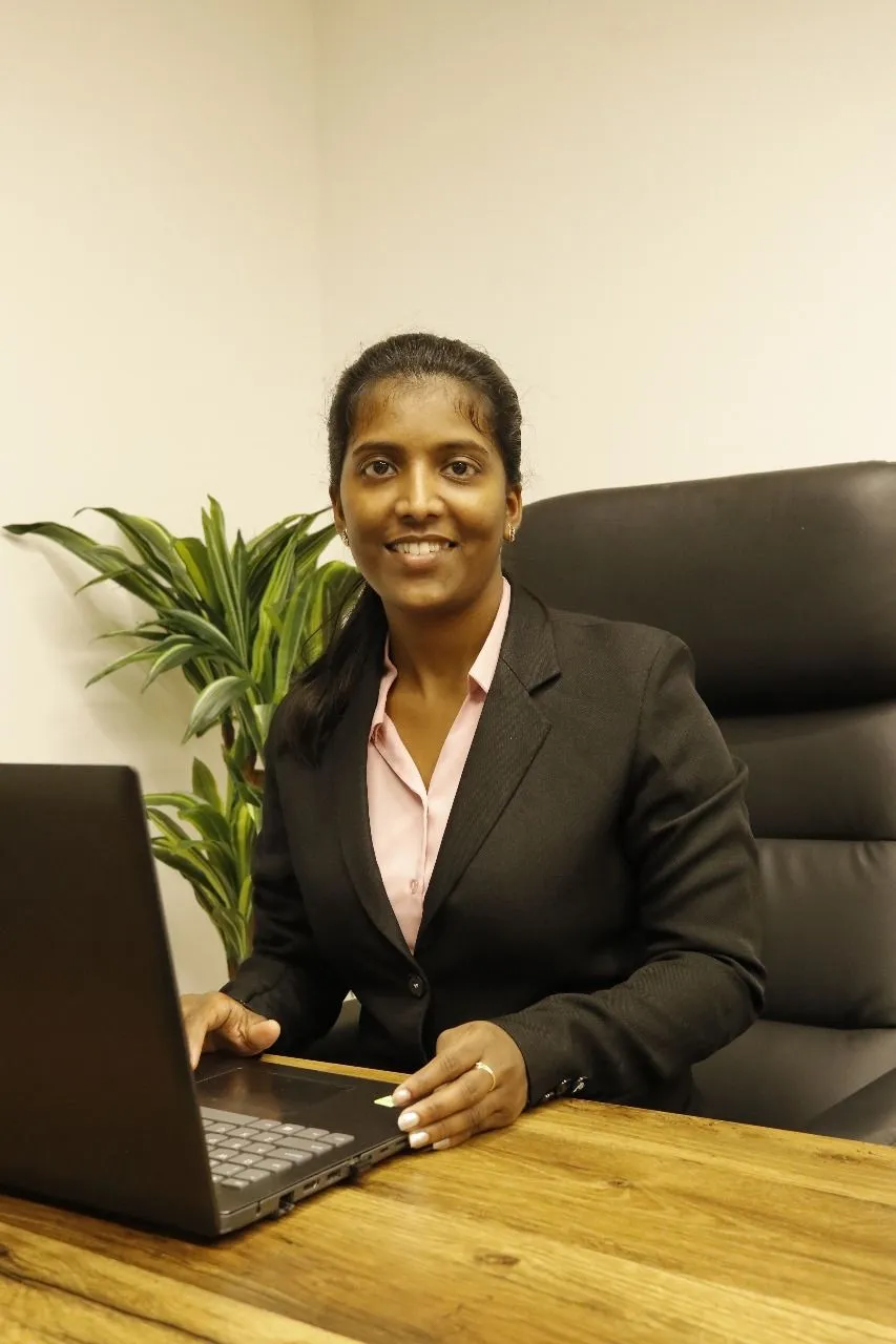 A professional woman in a business suit sits at her desk, focused on her laptop, embodying determination and productivity.