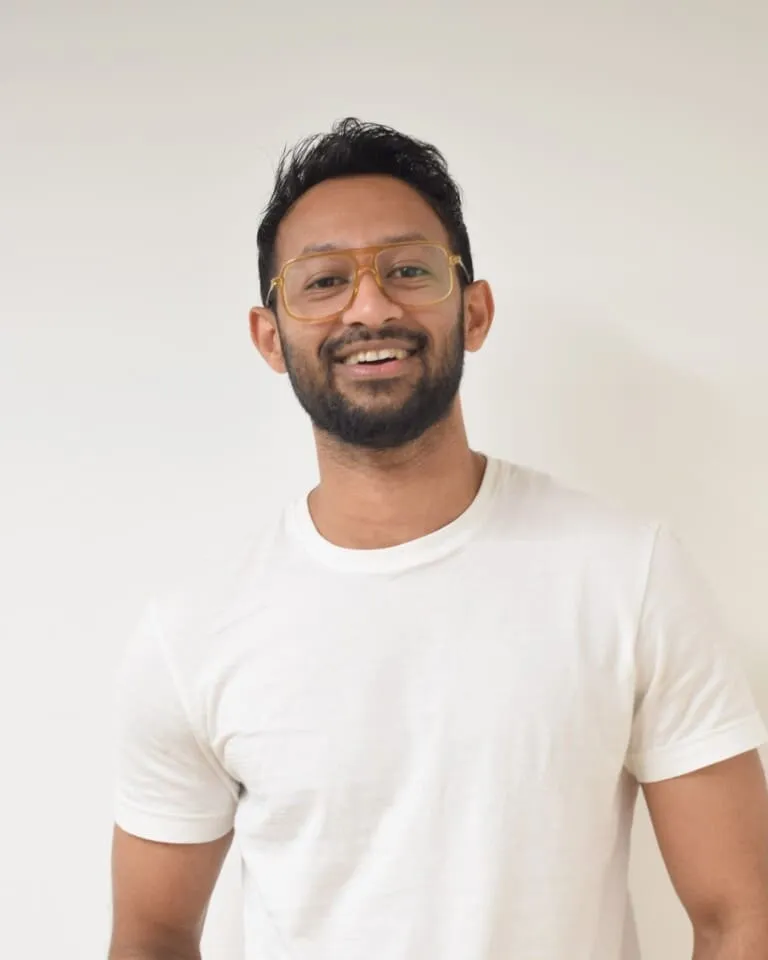 A bearded man with glasses smiles warmly at the camera, radiating a friendly and approachable demeanor.